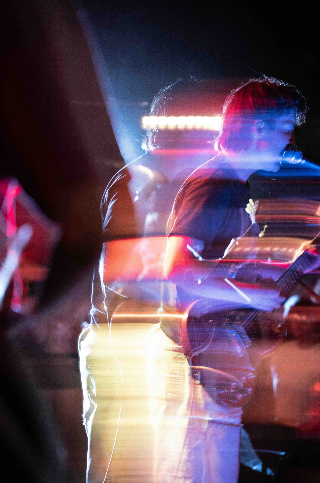 Two people playing guitar on a stage with colorful lights